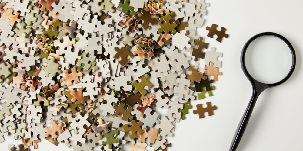 top view of magnifying glass and jigsaw puzzle pieces on grey