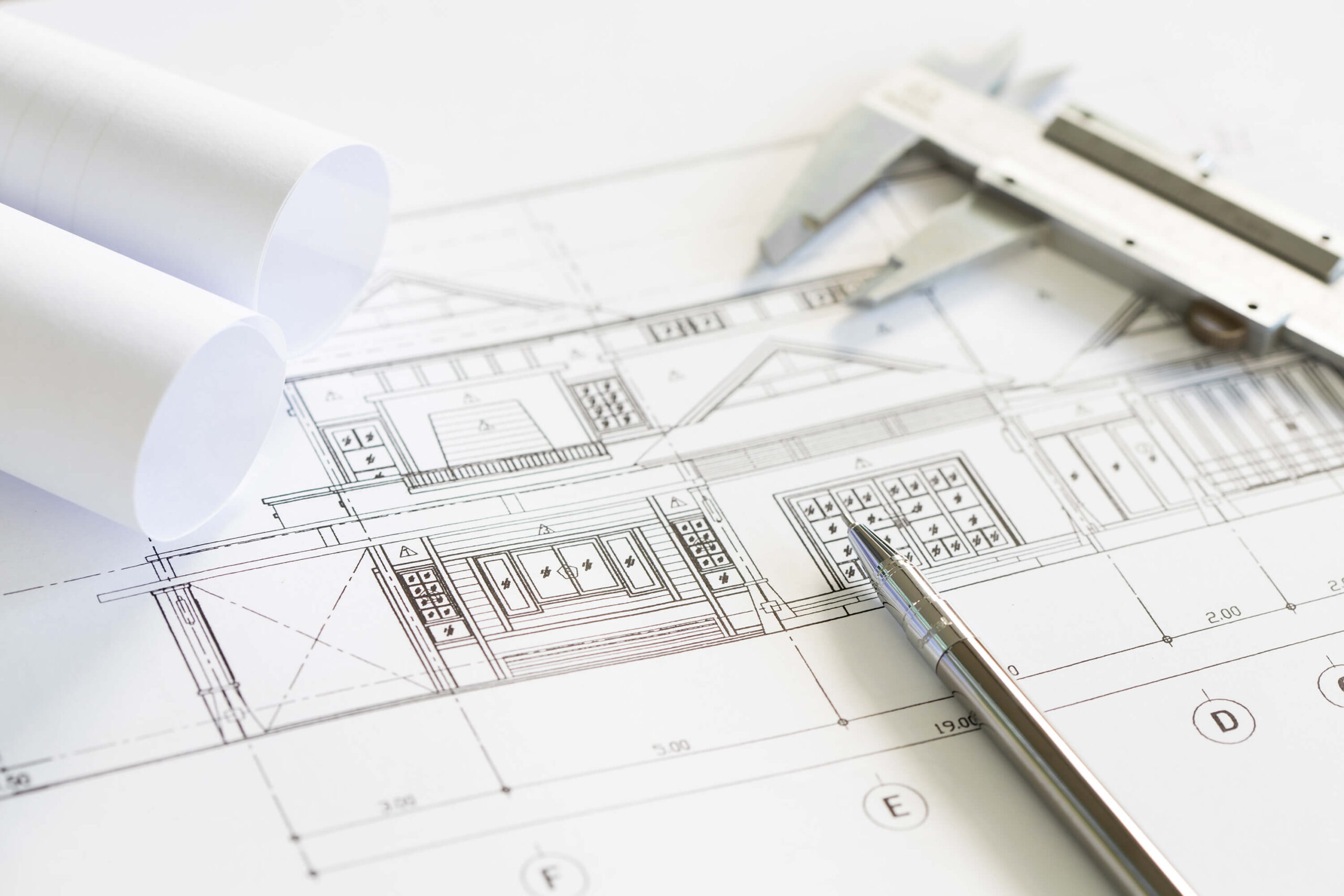 Architekturplan mit aufgerollten Plänen, einem Messschieber und einem Stift auf einem Tisch.